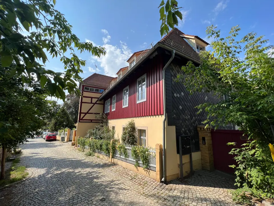 The house seen from the lane: half-timbered gable, oxblood-red wooden facade and slate wall
